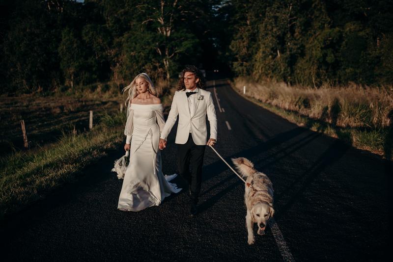 Real bride Hannah wears the Lauren gown; an off shoulder wedding dress with customised Nikki sleeves by Karen Willis Holmes holding labrador dog