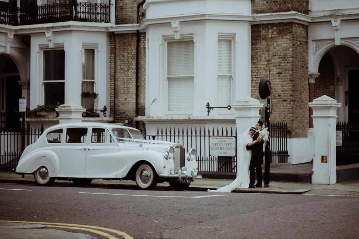 New couple hugging in front of vintage wedding car
