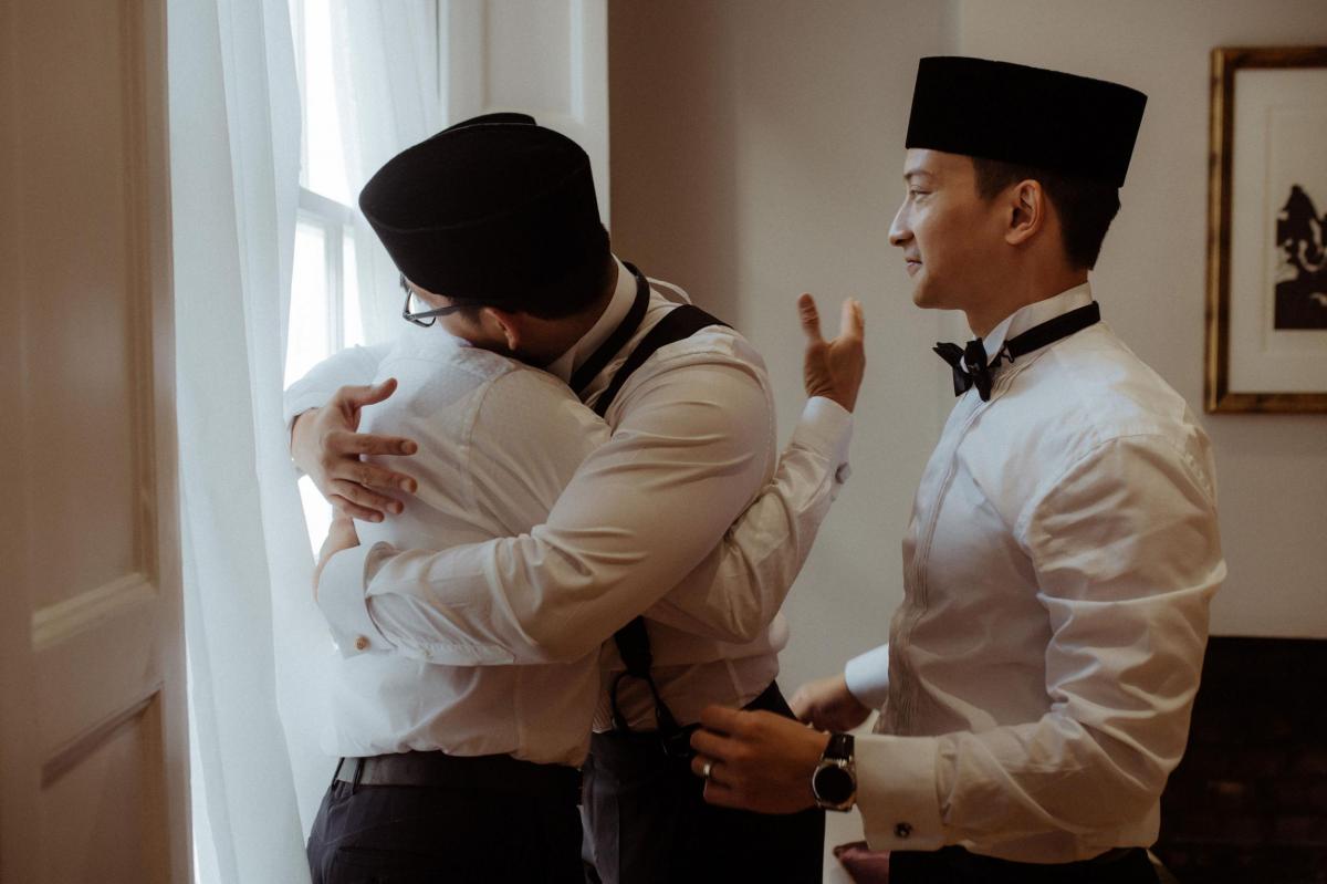 Groom and groomsmen hug in tuxedos at London wedding