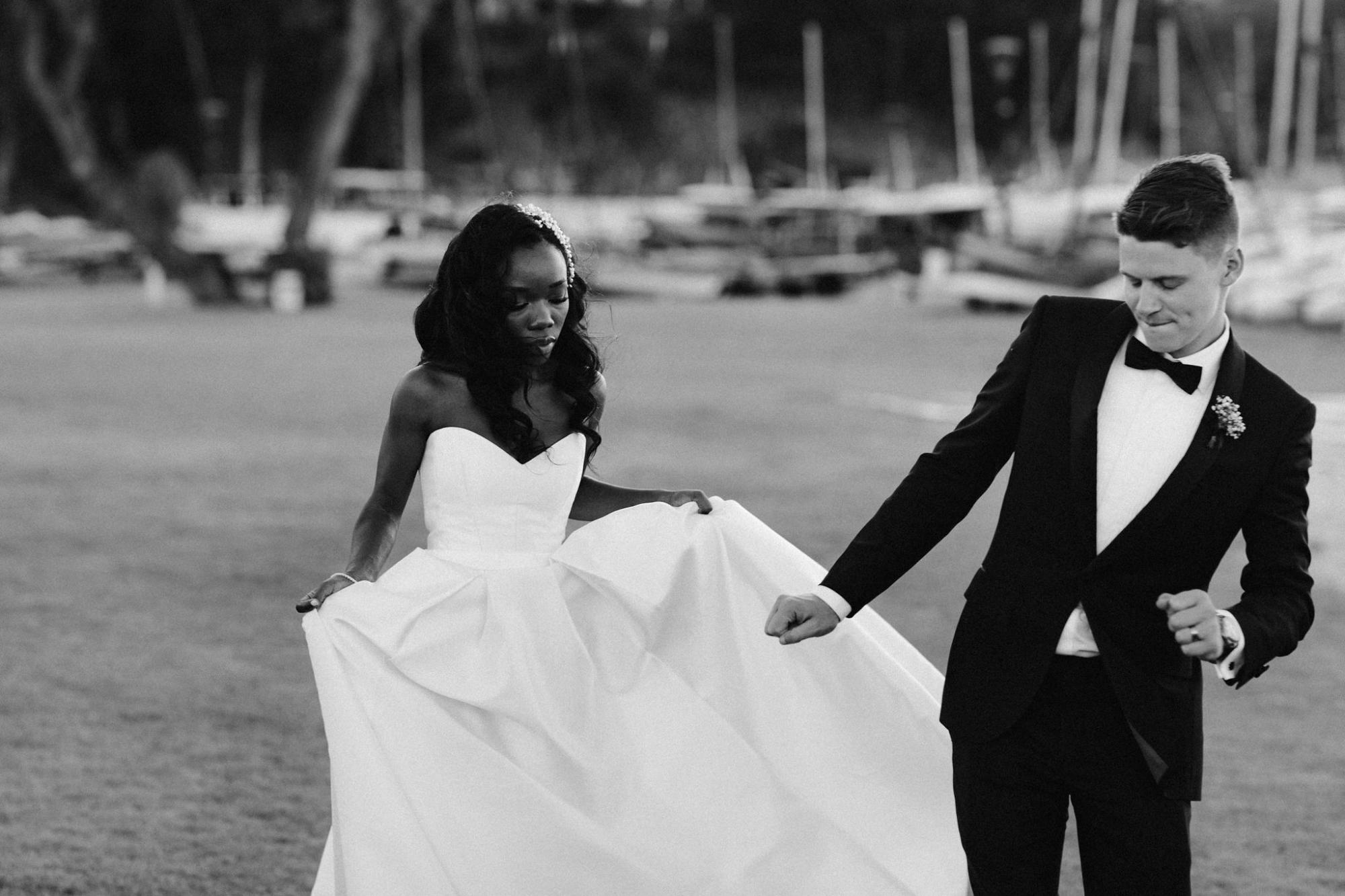 KWH Real bride Ancille and husband Dar stand on the beacha as he wraps his arms around her waist. She wears the timeless Kitty Melanie gown with pockets.