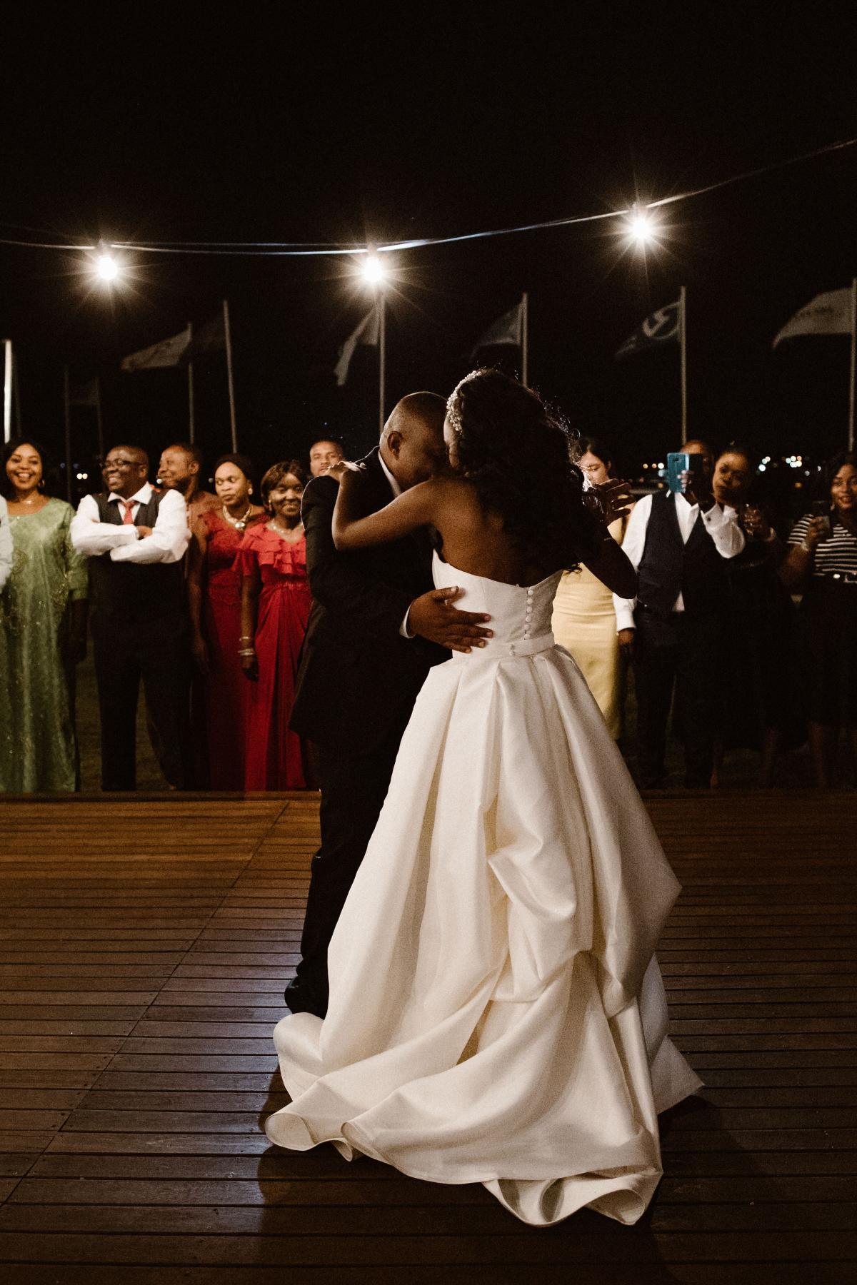 KWH real bride Ancille dances with her dad under the twinkeling lights. She wears the custom Kitty Melanie gown with a bustle in the back for dancing.