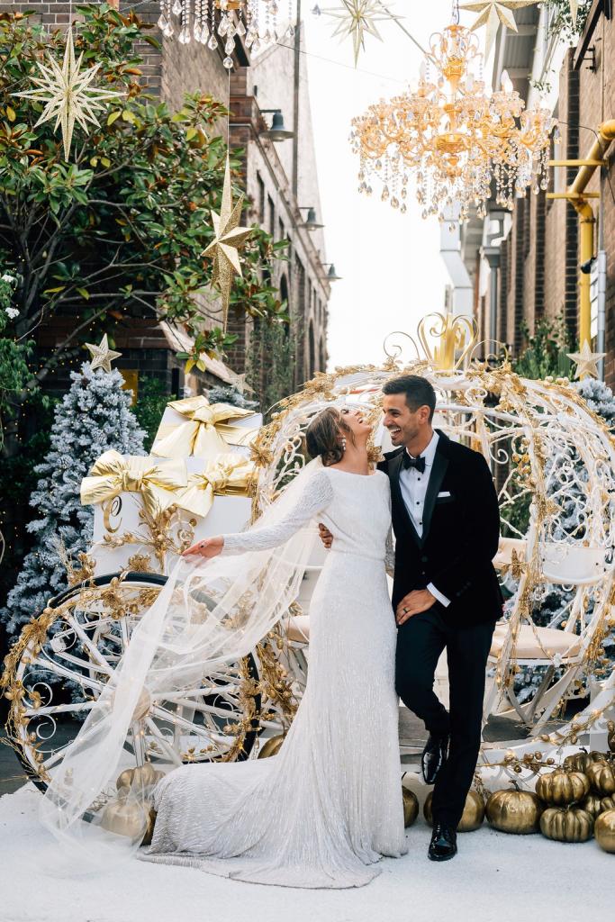Real bride Katrina in front of Cinderella style carriage at the grounds of Alexandria, wearing the Margareta gown; a long sleeve backless wedding dress by Karen Willis Holmes