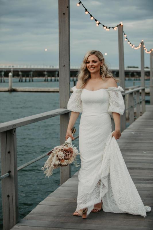Real bride Kacie-Lee wears the Vivienne gown; a puff sleeve lace wedding dress by Karen Willis Holmes to beach wedding with natural toned bridal blooms.