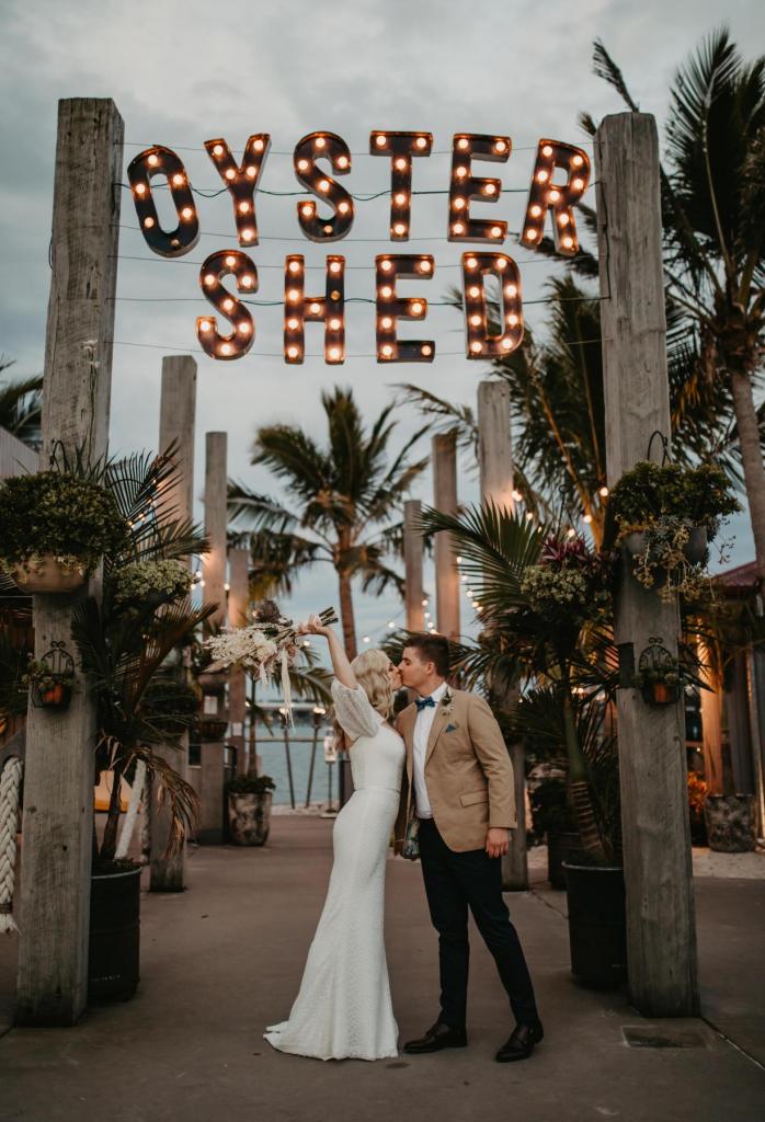 Real bride Kacie-Lee wears the Vivienne gown; a puff sleeve lace wedding dress by Karen Willis Holmes to beach wedding with natural toned bridal blooms.