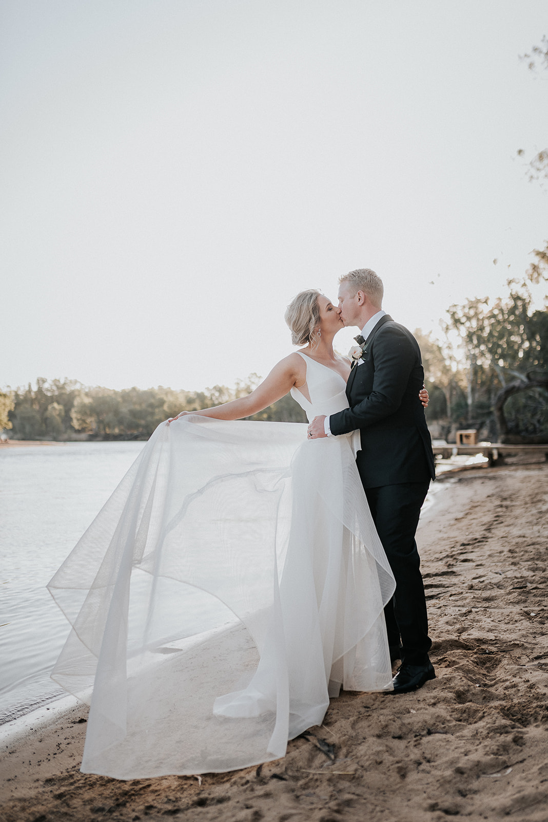 Real bride Samantha poses with her husband for wedding portraits, wearing the Aisha gown by Karen Willis Holmes; a V-neck A-line wedding dress made of honeycomb mesh fabric.