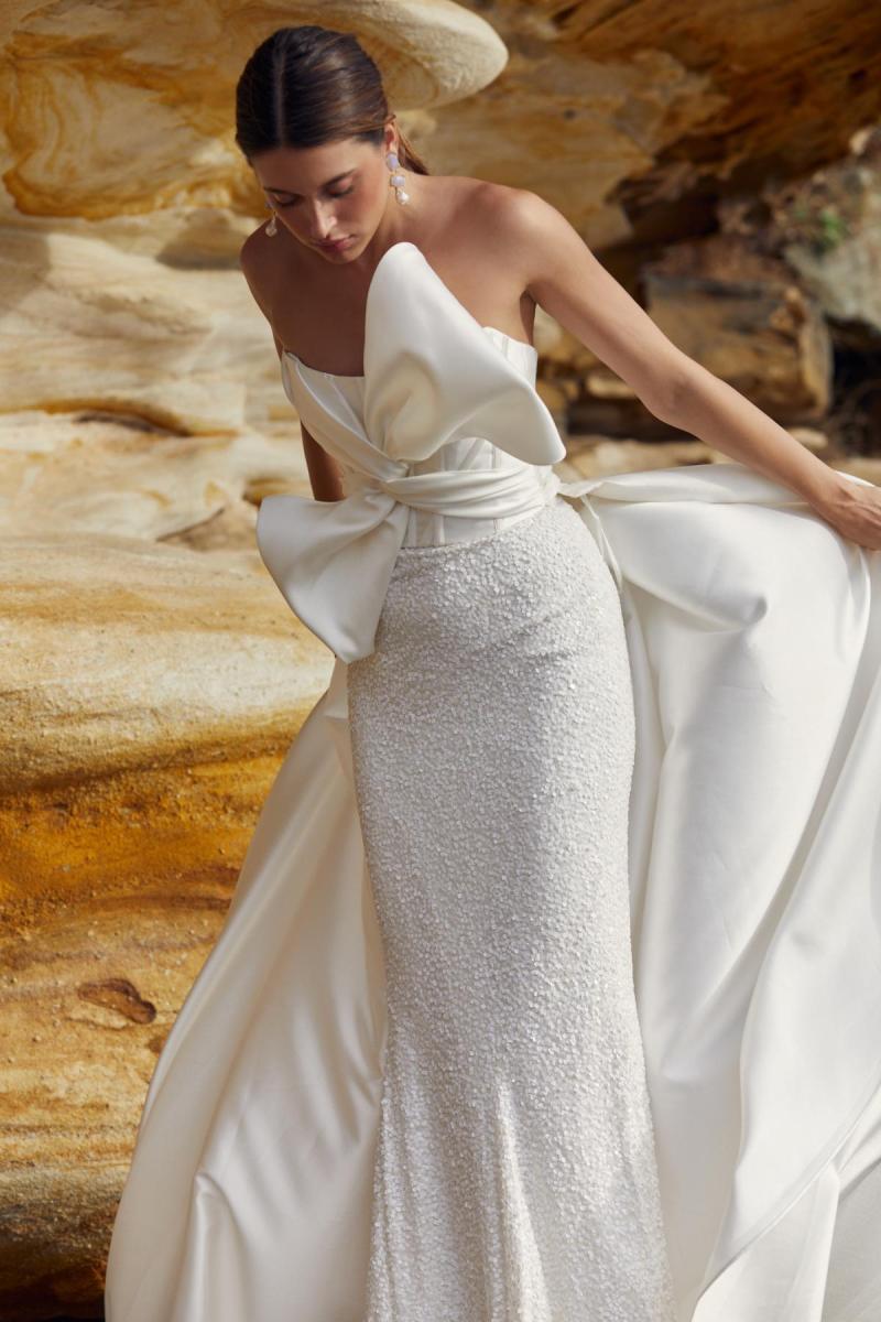 Ines & Avery is a modern statement wedding dress. Featuring a statement Bow on the bodice, paired with a beaded column shaped skirt and our detachable lindy train.