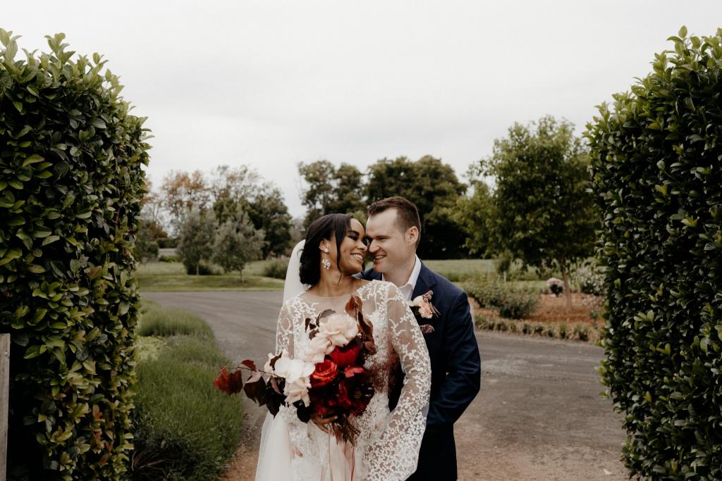 Real bride Saliya with husband at garden wedding, wearing the Pascale gown and Lucienne veil; a long sleeve boho lace wedding dress by Karen Willis Holmes.