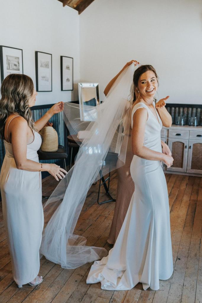 Real Bride Kate gets ready with her bridesmaids as they place her veil on her head. She wears the Arbella dress by KWH.