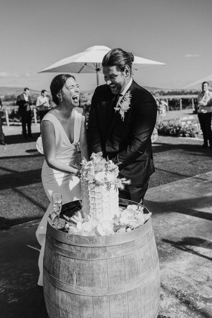 KWH real bride Kate laughs as she cuts the cake with her new husband. She dons the simple crepe Arabella gown.