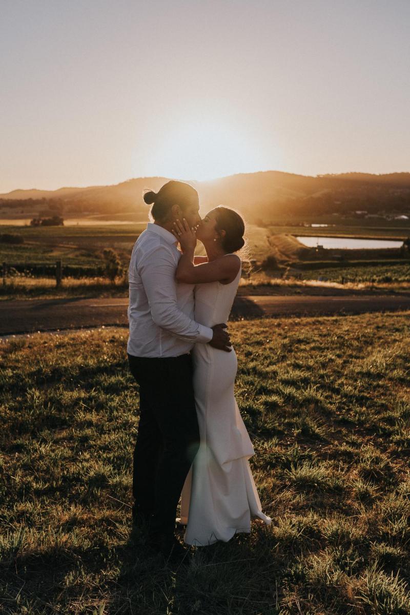 KWH Real bride Kate and Mik kiss in front of the sunset as she wears the modern, sleek, Arabella gown by KWH.