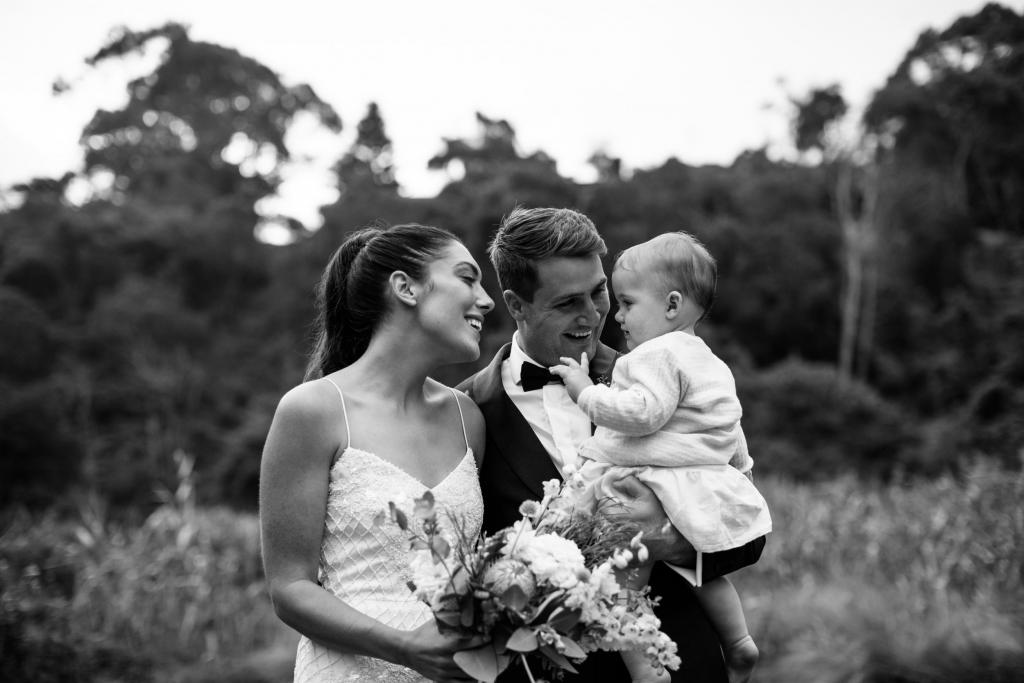Real bride Ruby and husband, Taylor, hold infant in stunning photo featuring her Darcy wedding dress by Karen Willis Holmes.
