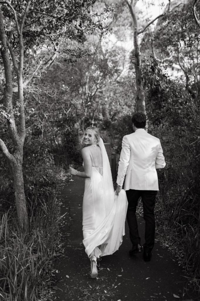 Real bride Riley and Wes walk throught the NSW forest with Wes grabbing her Sage gown's train by KWH.