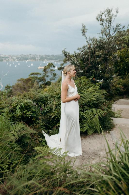 Real bride Riley stands in her sleek Sage gown by KWH with the ocean in the background.