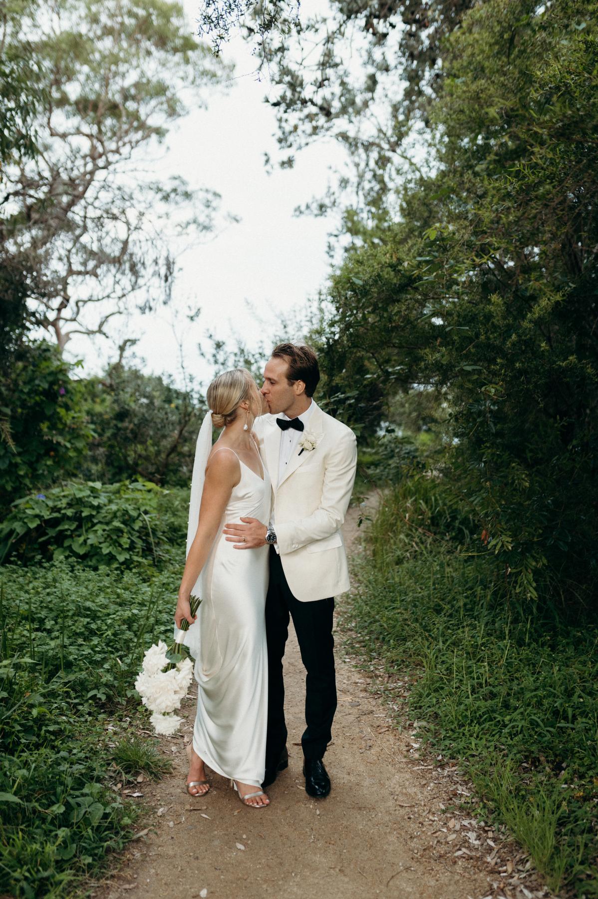 Real bride Riley and husband, Wes, kissing in the NSW woods in her Sage dress; a modern fitted wedding dress.