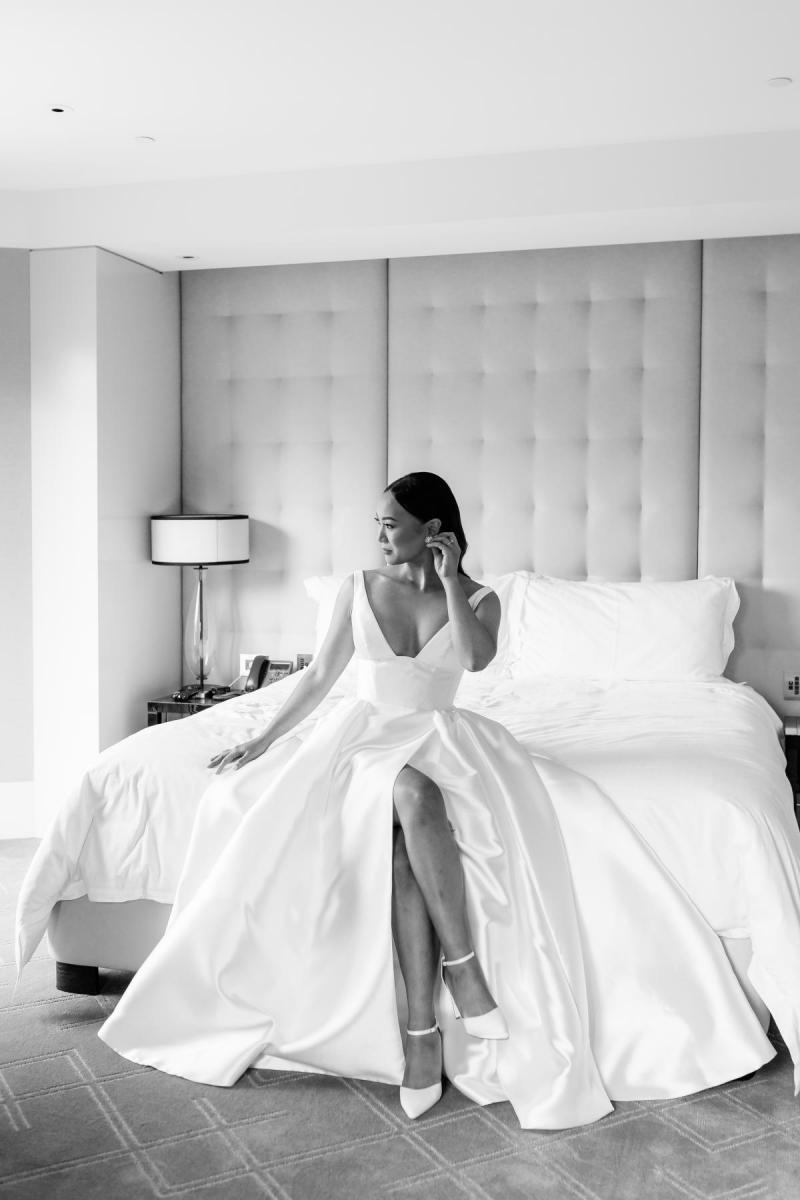 Real bride Anna sitting on the hotel bed in her stunning Taryn Camille gown by KWH. It has a long side split.