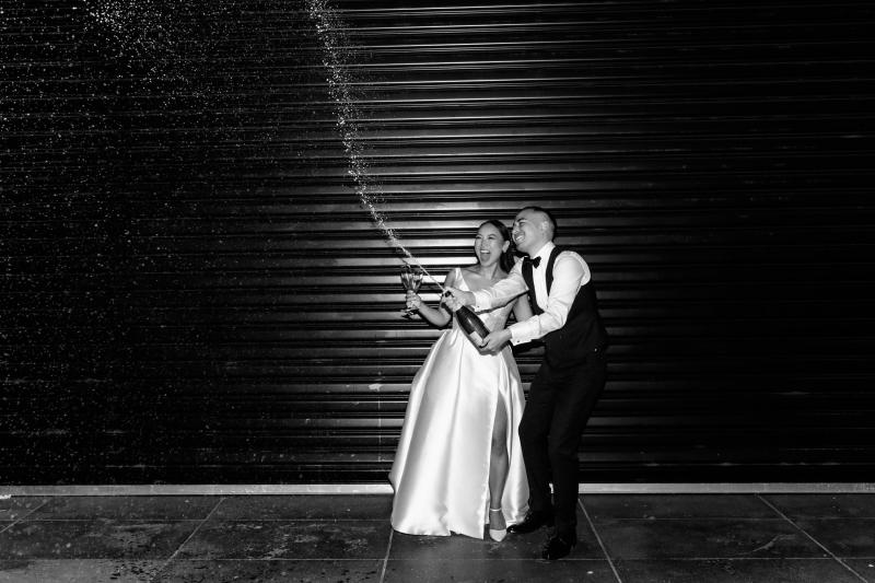 KWH real bride Anna and Matt celebrate by popping champagne. She wears the effortless Taryn Camille gown with twill material.