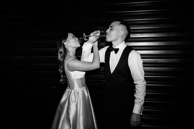 KWH real bride Anna and Matt sip champagne in this Black and White photo featuring her Taryn Camille gown with firm bodice and aline skirt.