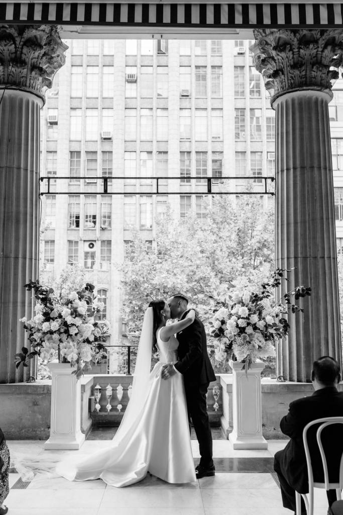 B&W photo of real bride Anna kissing her new husband at the alter while wearing her Taryn Camile gown by Karen Willis Holmes featuring an aline skirt and modern neckline.