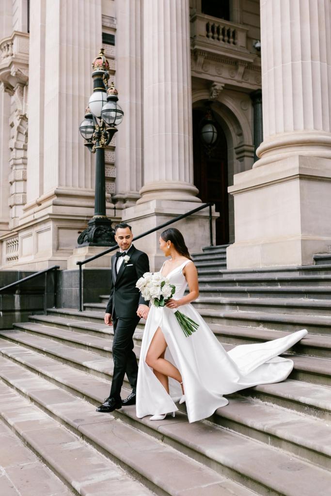 KWH real bride Anna walking down the stairs in her Taryn Camille gown with high leg split and modern neckline.