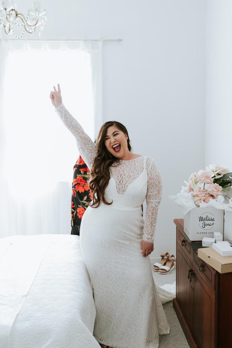 KWH bride Jarna gets pumped up in her bridal suit for her outdoor wedding while wearing Karina; a simple, lace, wedding dress with plunging neckline.
