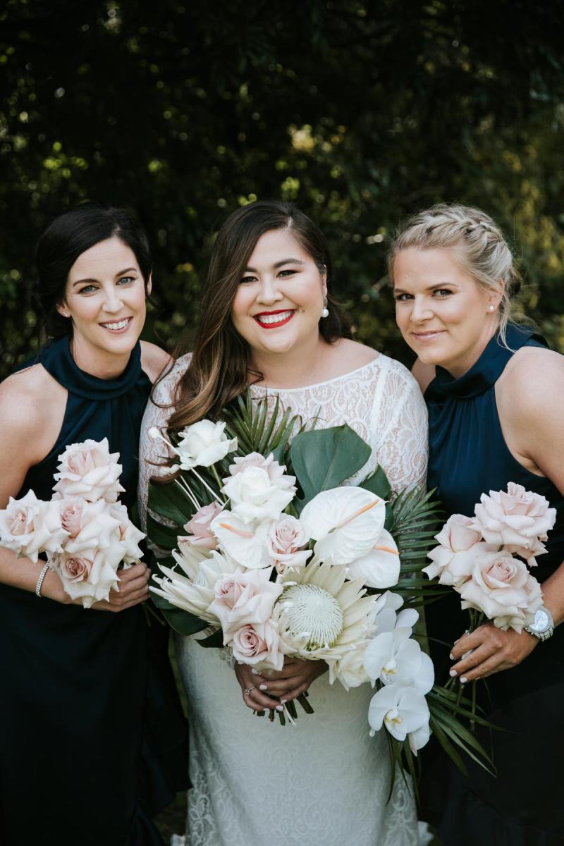 Bride's maids gather around KWH bride Jarna as she shines in her Karina dress that features a modern U-shaped neckline with illusion lace boat neck overlay.
