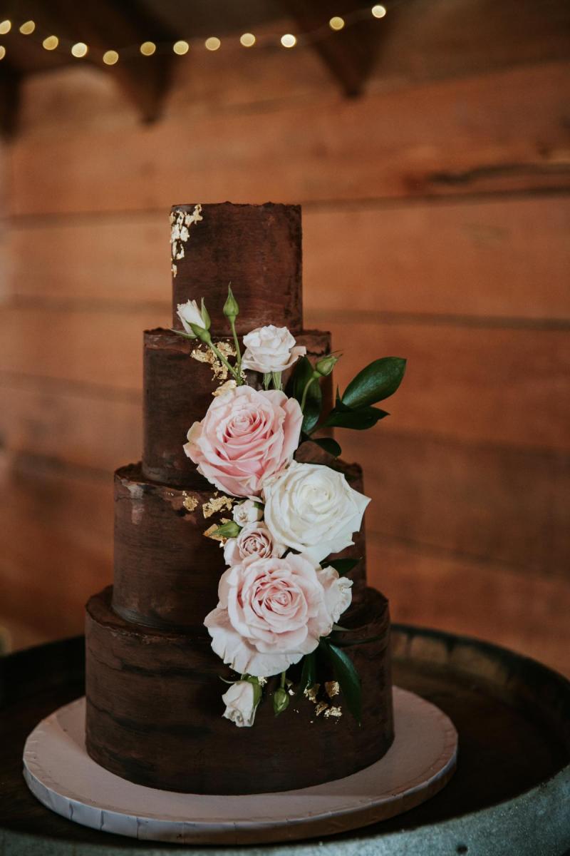 A four tier brown wedding cake with light pink roses sits on the table at Jarna and Aden's intimate countryside wedding.