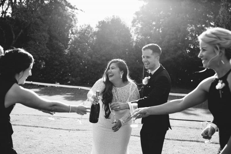 KWH real bride Jarna popping champagne with friends and new husband at modern boho wedding.
