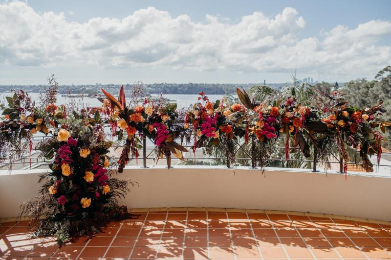 KWH real bride Eliza's florals draping over the railing at their venue with bold deep red and greens.