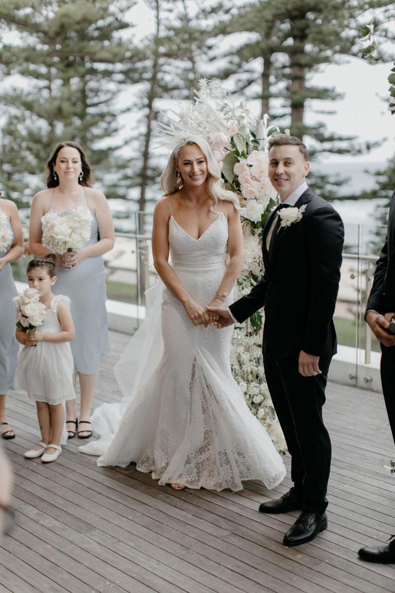 Real bride Nicole stands at the alter with her fiance as they exchange vows. She wears the simple Justine gown with detachable Odette train.