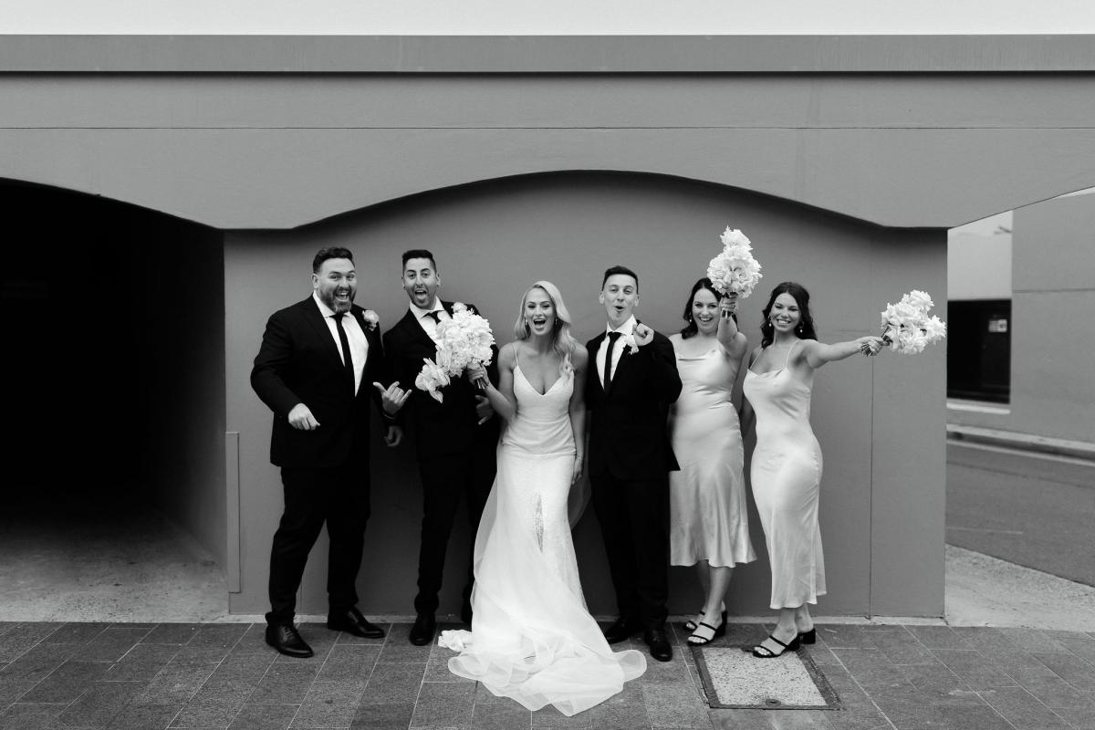 KWH real bride Nicole with her bridal and groom's party in this B&W image. She wears the lace Justine gown with raw edge.