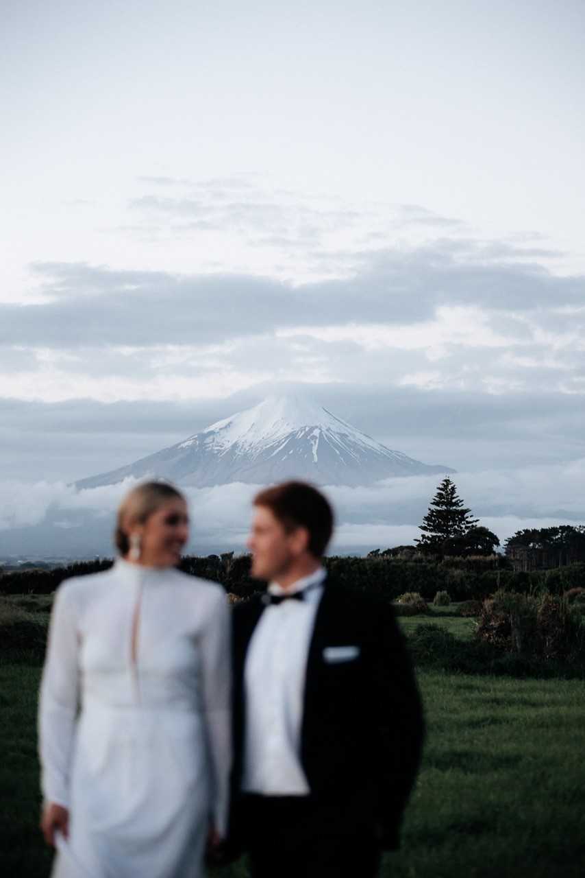 KWH real bride Hannah and Angus stand in front of Mt. Taranaki in her custom gown made by her brother.