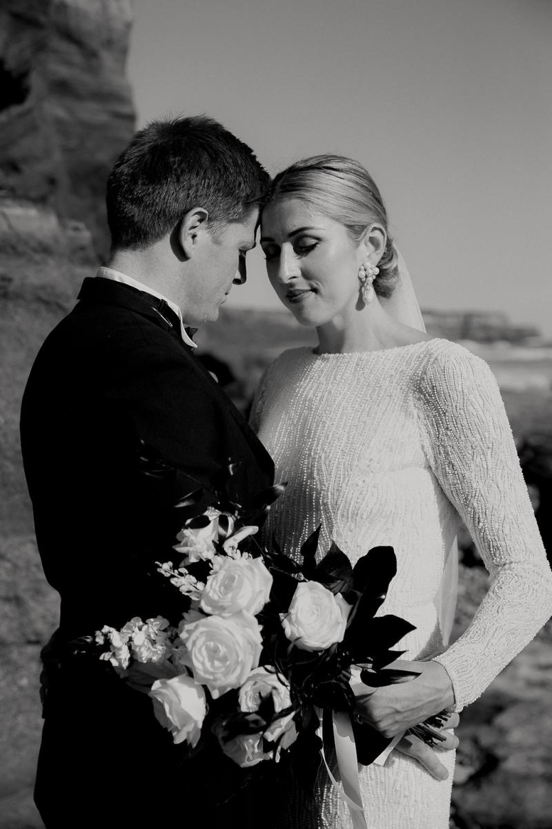 Black and white photo of KWH real bride Hannah and new husband Angus having a moment on the beach. She wears the high neckline Margaretta dress with long sleeves.