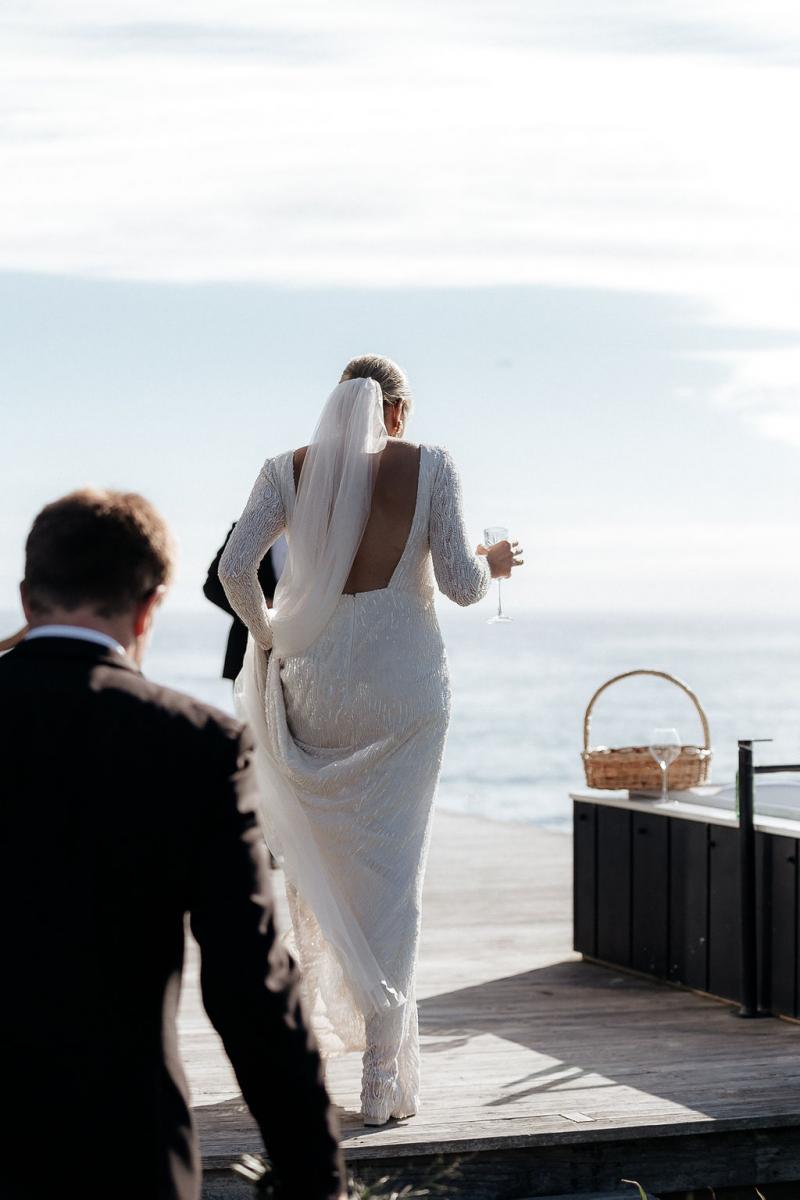 Real bride Hannah wears the short train Margareta wedding dress by KWH as she walks onto a platform by the sea