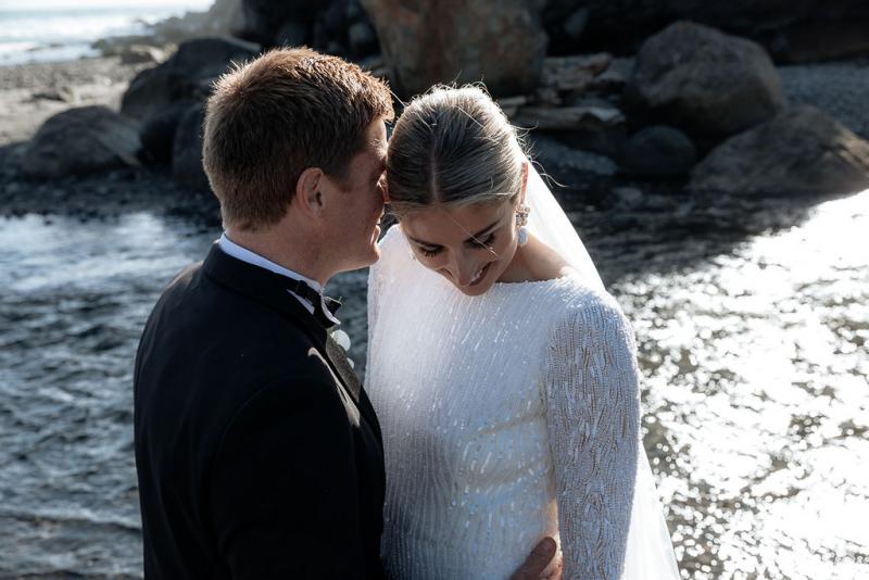 Black and white photo of KWH real bride Hannah and new husband Angus having a moment on the beach. She wears the high neckline Margaretta dress with long sleeves.