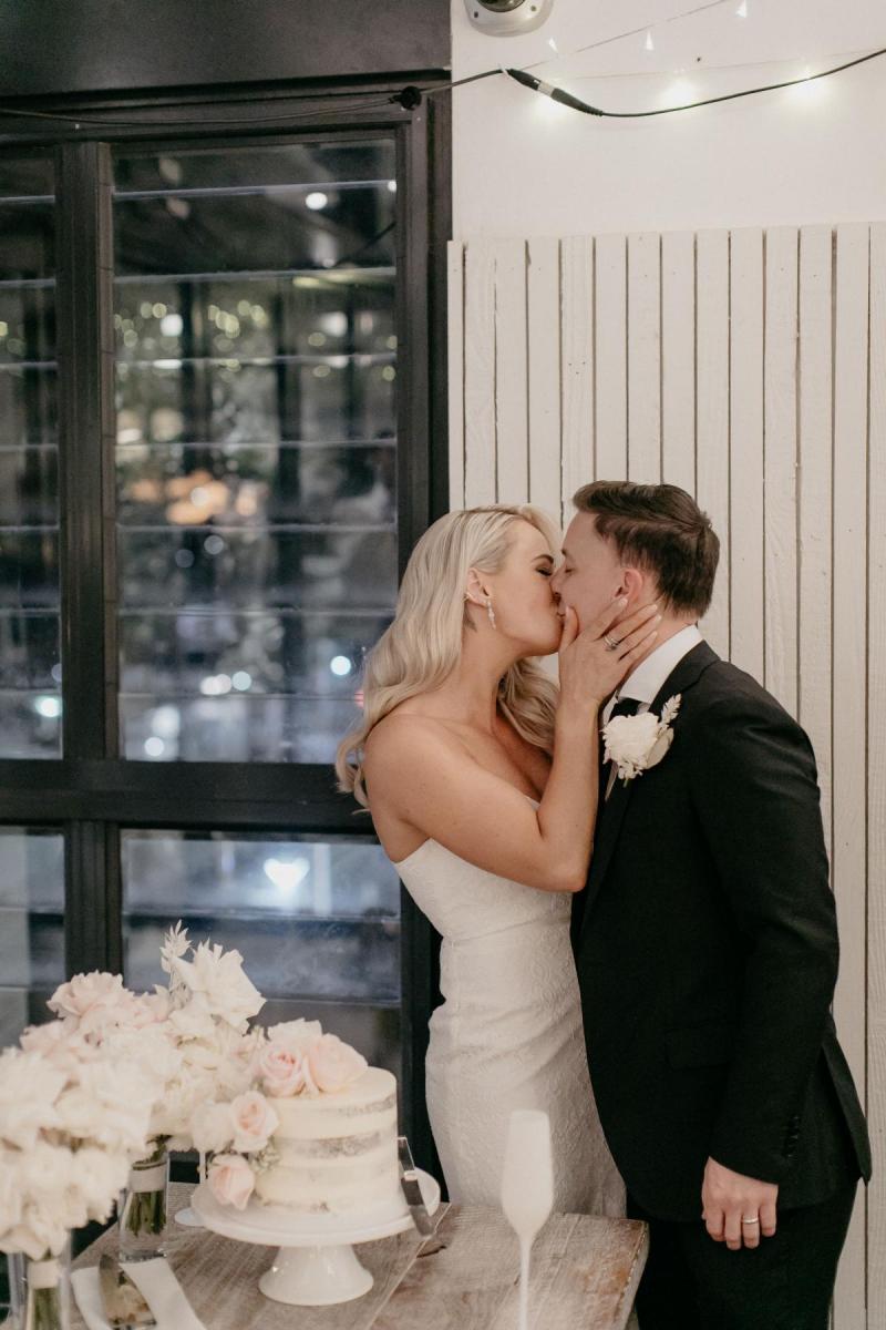 KWH real bride Nicole kissing her groom after the cake cutting. She wears the lace, shoe string strap Justine gown.