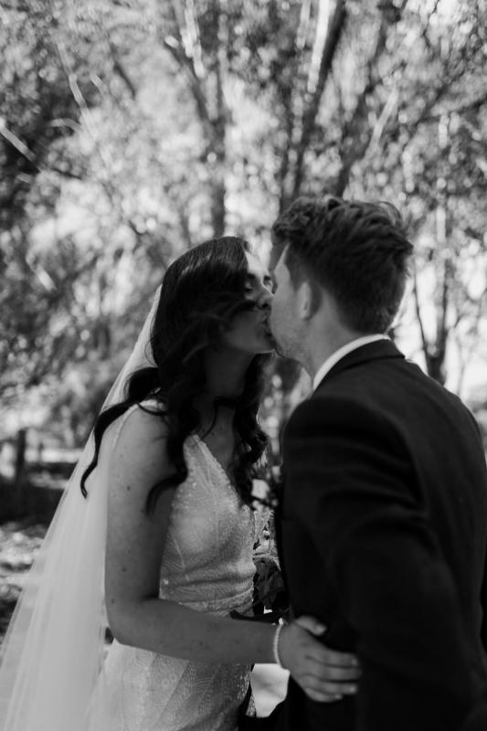 Real bride Amber and Stewart kissing in this blak and white photo. She wears the fit and flare classic Olympia wedding dress by KWH.