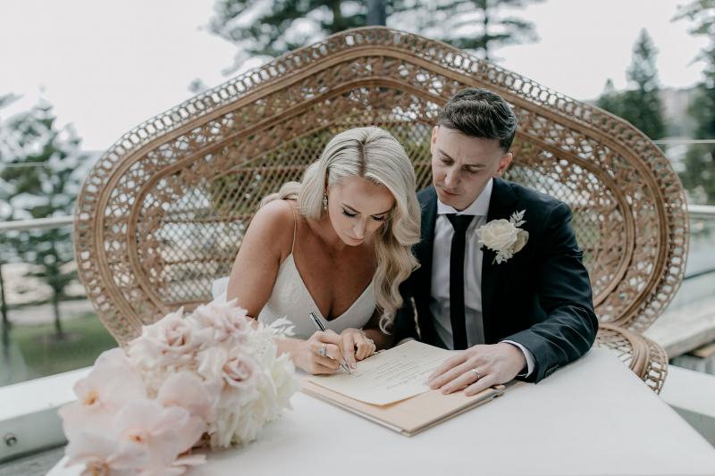 KWH real bride Nicole and Chris sign their marriage certificate in a rattan grand chair.
