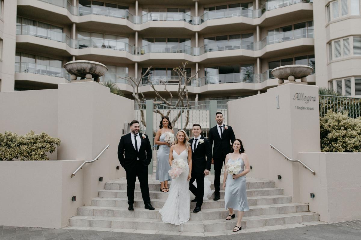 KWH real bride Nicole with her bridal party on the stairs of the hotel. She wears the minimalist Justine gown.