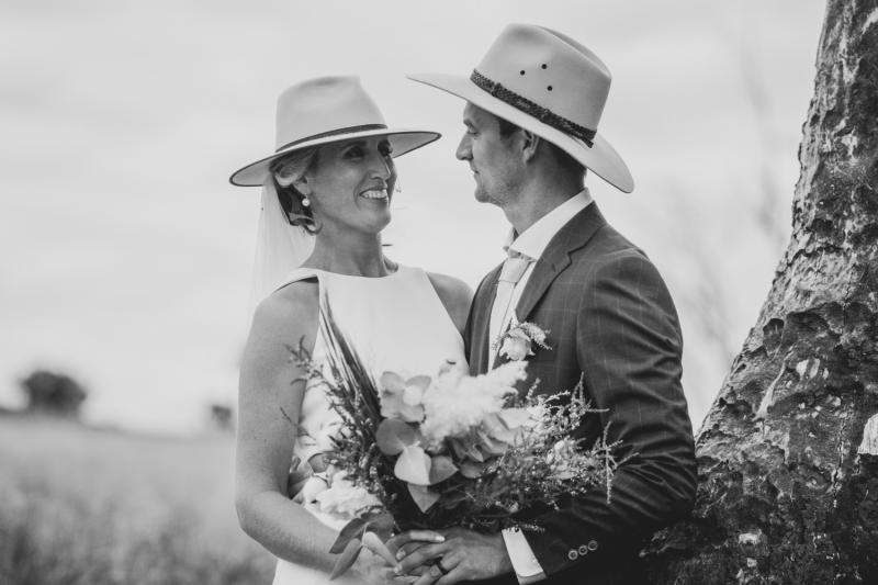 B&W photo of Real Bride Angela smiling at her husband while holding her native bouquet and wearing her high neck Bridget gownl.