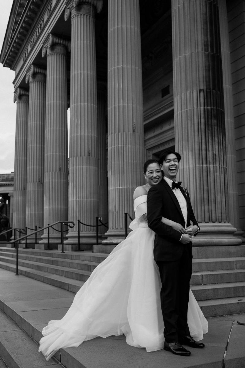 B&W photo of KWH real bride Sarah and Brian on the steps of the art gallery. She wears the custom organza and twill Kitty Joni gown.