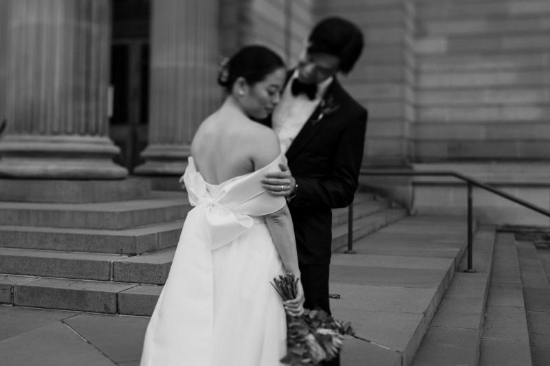 KWH real bride Sarah and Brian hugging on the gallery steps. This B&W image shows off the lace up back of her Kitty Joni gown.