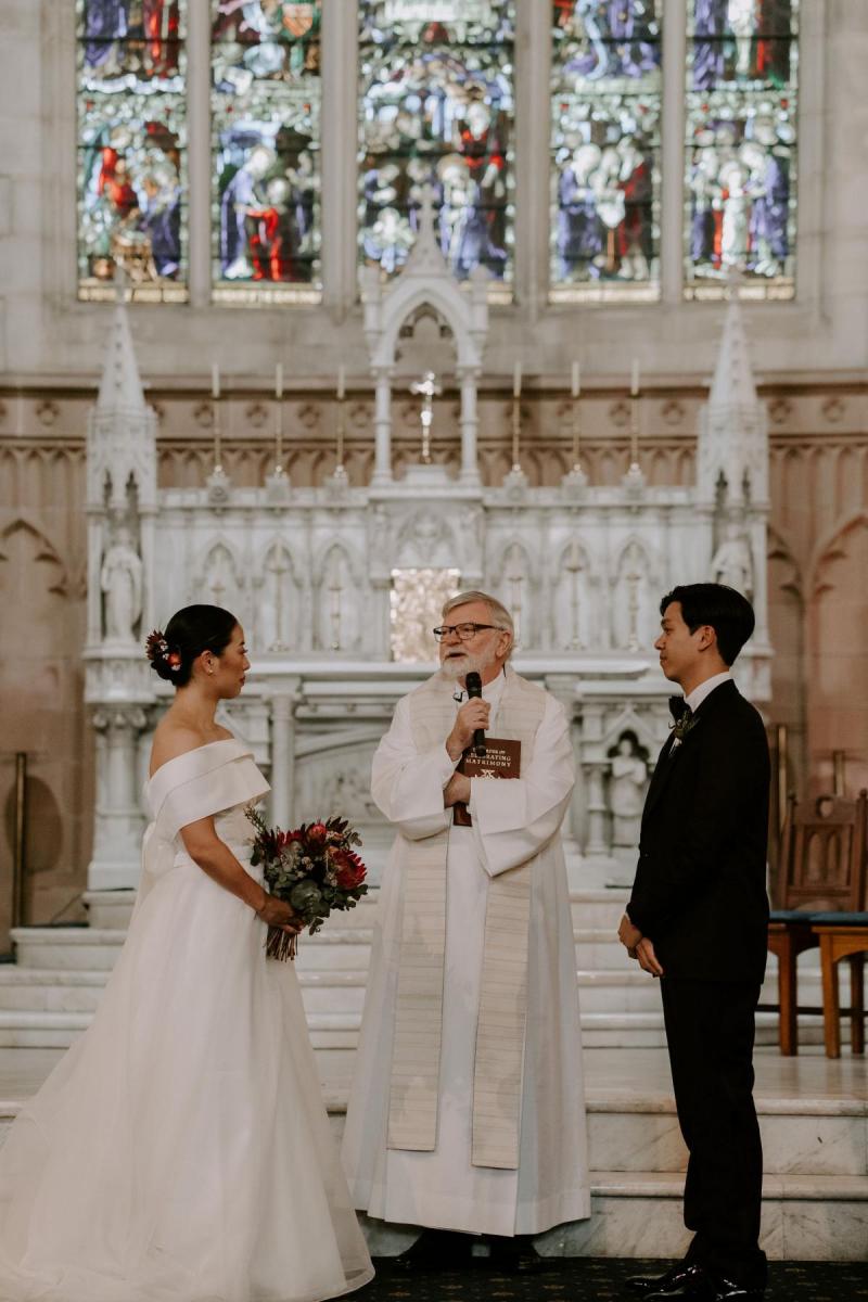 KWH real bride Sarah and Brian stand at the alter with their Priest to exchange vows. She wears the twill and tulle Kitty Joni gown.
