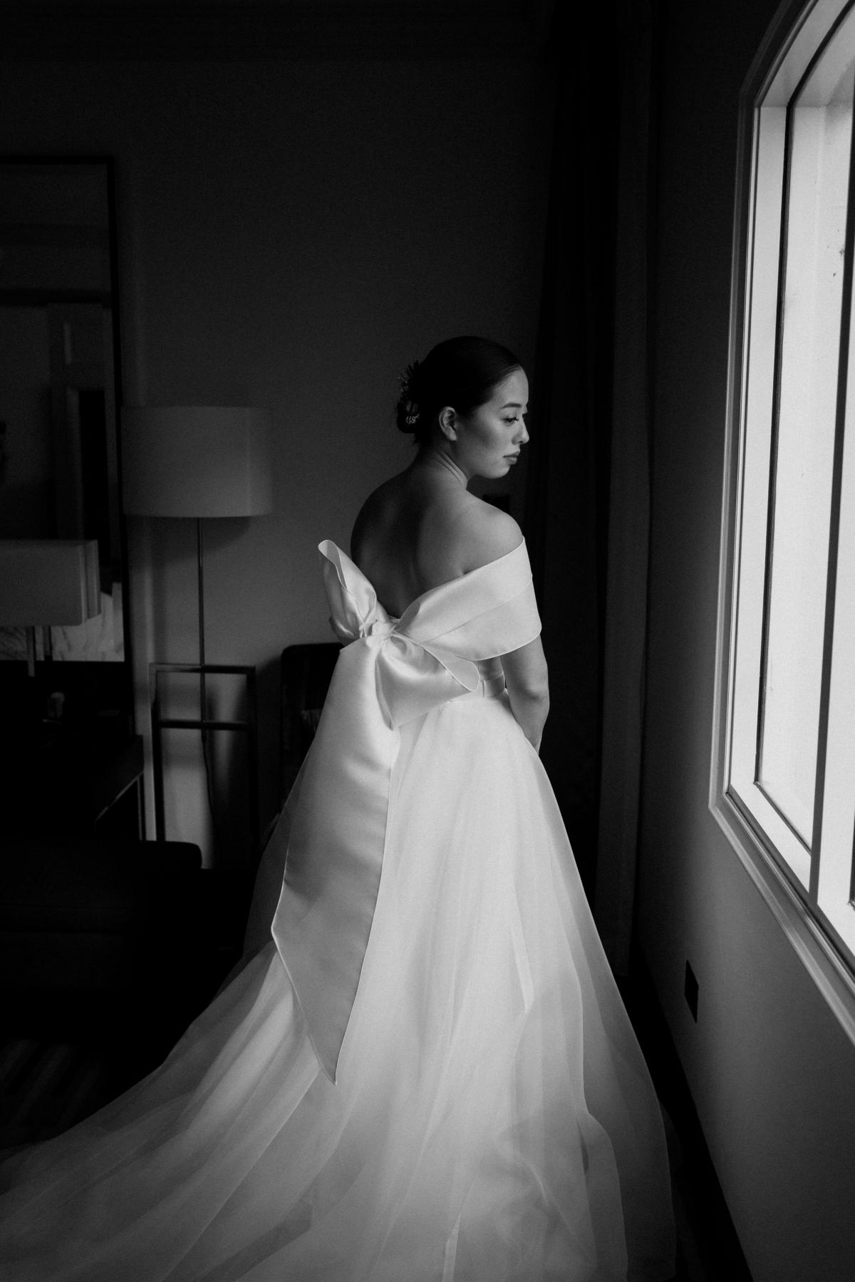 KWH real bride Sarah standing by the window light in her Kitty Joni gown with Twill sash around her sholders.