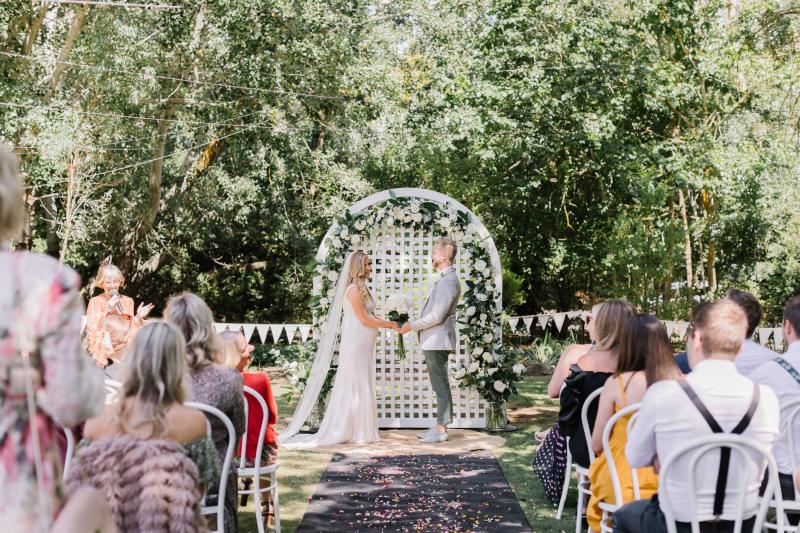 KWH real bride Bec and Nick stand at a white lattic alter. She wears the beaded Olympia wedding dress with organic pattern.