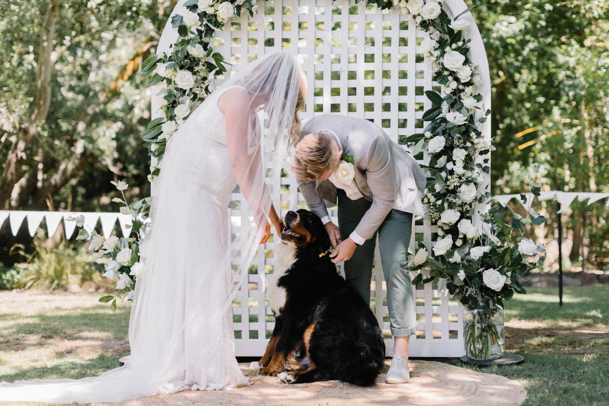 KWH real bride Bec and Nick stand at a white lattic alter. She wears the beaded Olympia wedding dress with organic pattern.