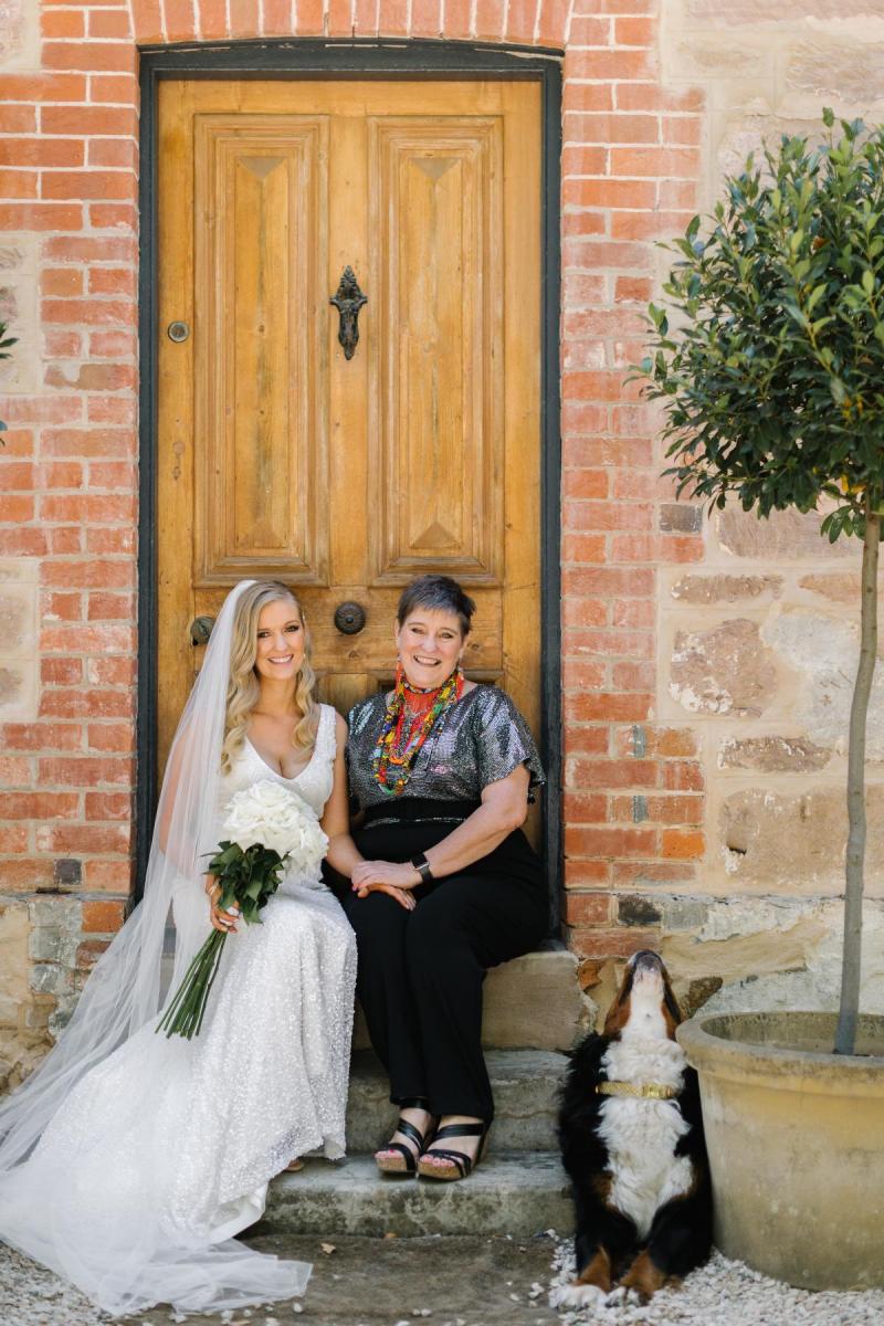 KWH real bride stands with her bridesmaids in front of a door. She wears the fit and flare Olympia beaded wedding dress.