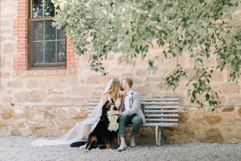 KWH real bride Bec kisses Nick on a bench. She wears the ivory beaded Olympia wedding dress.