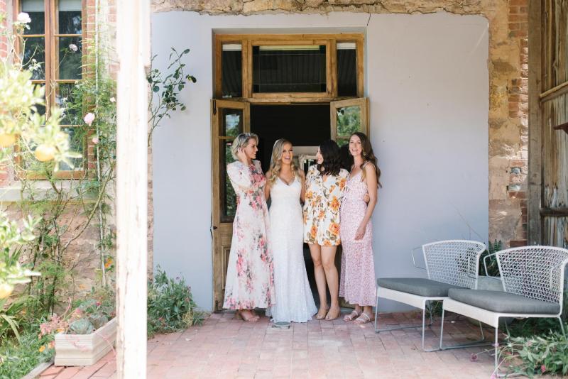 KWH real bride stands with her bridesmaids in front of a door. She wears the fit and flare Olympia beaded wedding dress.