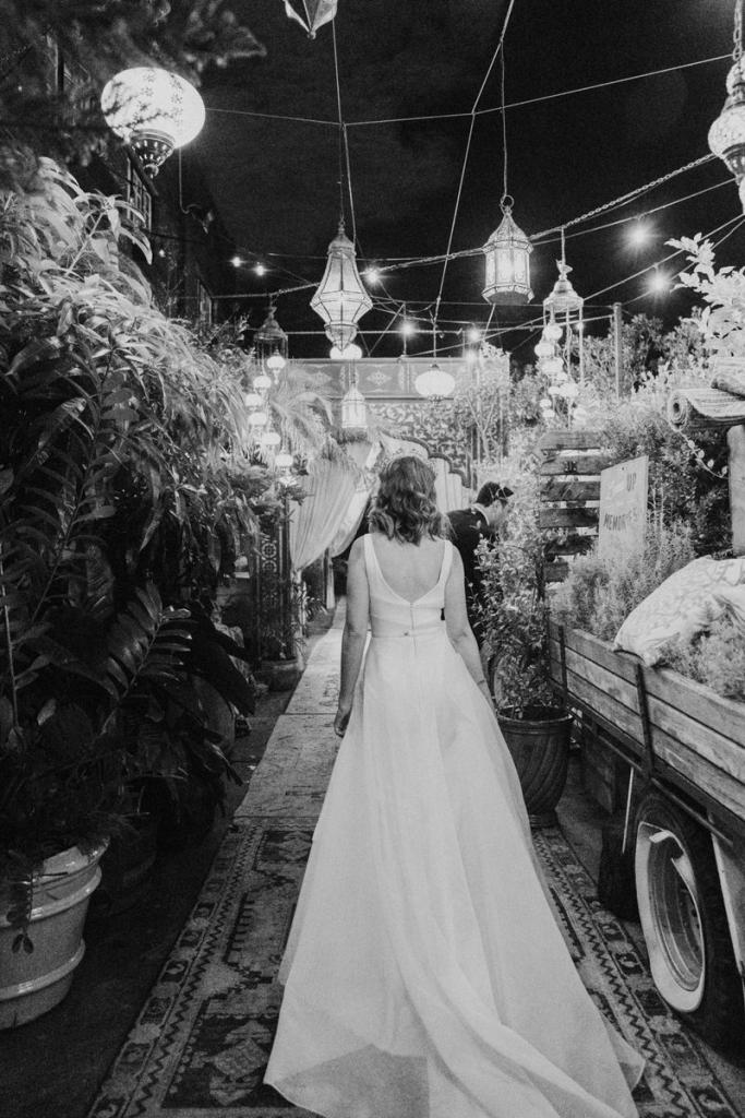 B&W photo of KWH real bride Talia walking through her reception in her Aisha wedding dress with aline skirt and low back.