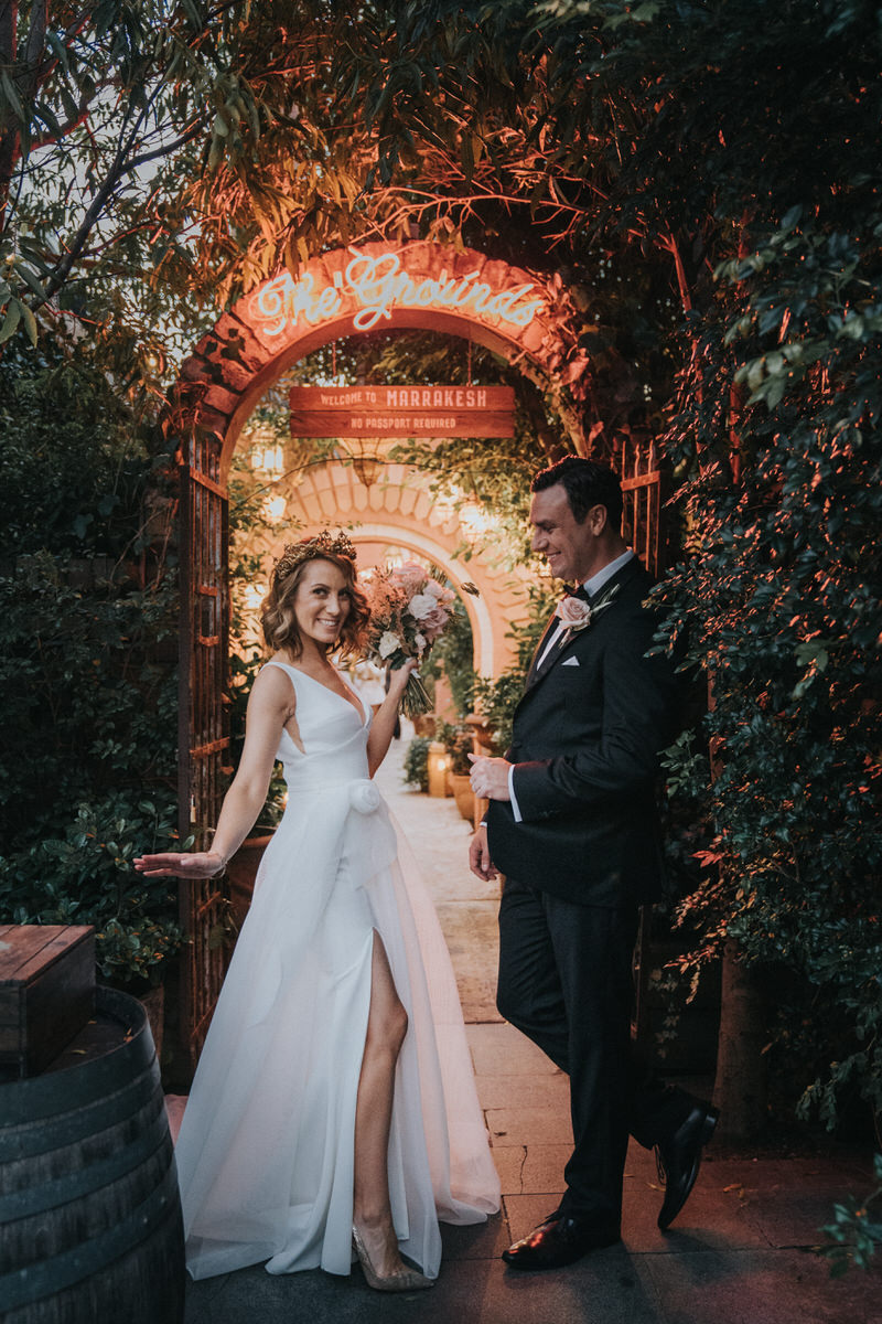 KWH real bride Talia standing under a neon sign at her reception. She wears the modern Aisha wedding dress with leg split in her aline skirt.